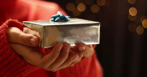 Close-up of hands holding a silver gift box with a blue bow, festive bokeh Stock Footage 339071497