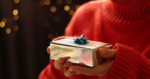 Close-up of hands holding a silver gift box with a blue bow, festive bokeh Stock Footage 339072096