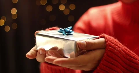 Close up of hands holding a silver gift box with a blue bow, festive bokeh Stock Footage 339072181