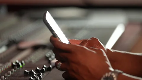 Close-up of hands holding smartphone with audio mixing console in background Stock Footage 331417938