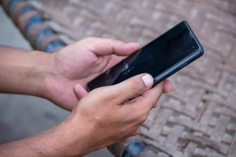 Close up of hands holding smartphone while sitting on traditional charpai Photos