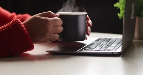 Close-up of hands holding a steaming mug next to a laptop, working from home Stock Footage 339072476