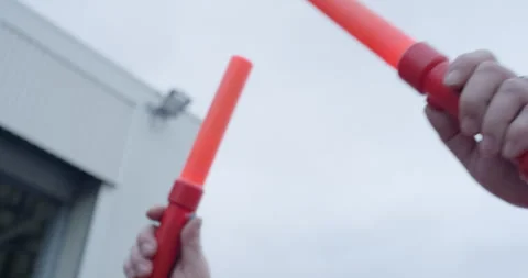 Close up of hands holding two orange illuminated aviation signal wands Stockbeeldmateriaal 329550848