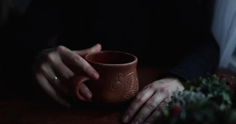 Close-up hands hug and twist a brown ceramic mug on a wooden table Stock Footage 129710136