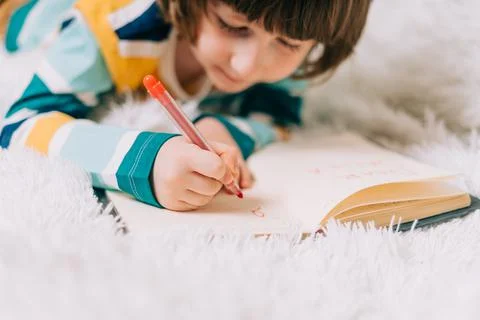 Close up hands of Kid boy, lying on couch and writing letter in note pad to dear Stock Photos