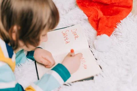 Close up hands of Kid boy, lying on couch and writing letter in note pad to dear Stock Photos