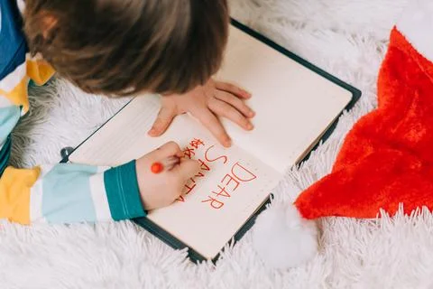 Close up hands of Kid boy, lying on couch and writing letter in note pad to dear Stock Photos