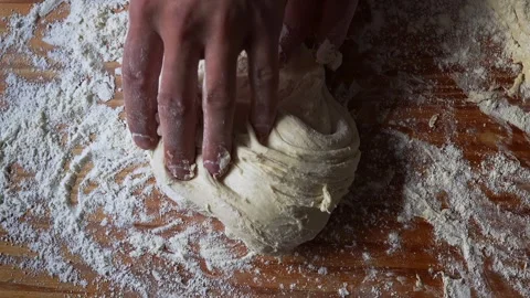 Close-up of hands kneading raw dough on a floured wooden surface, stretching and Stock Footage 303889580