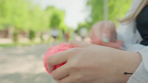 Close up of hands knitting with pink yarn in park during daylight showing Stockbeeldmateriaal 345841264