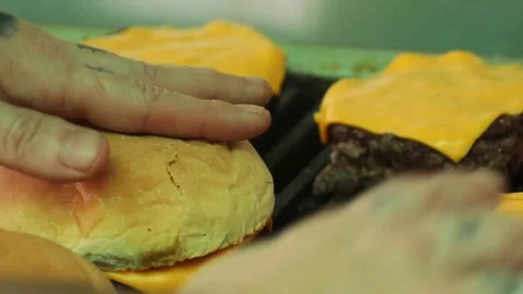 Close up of hands laying buns on top of cheeseburgers on a hot grill Stock Footage 127716031
