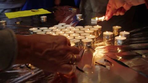 Close-up of hands lighting tea candles on a reflective surface. Group Stock Footage 304727953