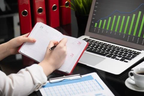 Close-up of hands making notes in diary next to tablet computer Foto stock
