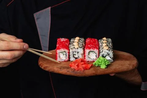 Close-up of the hands of a Man chef in a black uniform holding a wooden tray Stock Photos