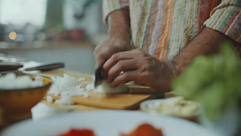Close-Up of Hands of Man Cutting Onion on Wooden Board at Kitchen Table Stock Footage 303008356
