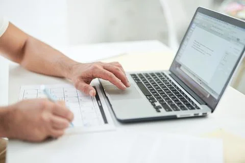 Close up of hands of man using his laptop and marking days in calendar while Stock Photos