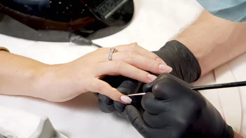 Close-up of the hands of a master in black gloves applying gel polish on the Stock Footage 150865501