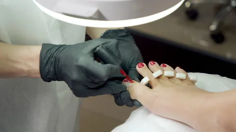 Close-up of the hands of a master in black gloves applying red gel polish to the Stock Footage 150865798