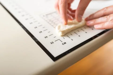 Close-up of hands measuring the length of a piece of dough on a kitchen mat with Stock Photos