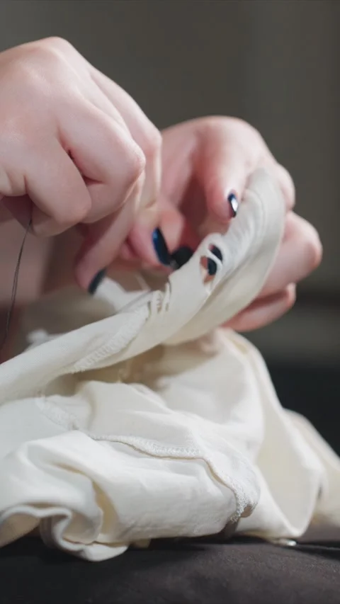 Close up hands mending torn white fabric with needle and thread featuring sewing Stock Footage 346796072