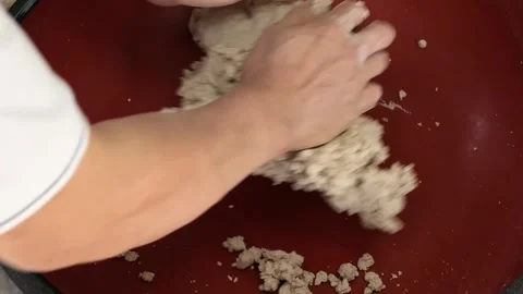 Close-up of Hands Mixing and Kneading Textured Raw Dough or Material in a Red Bo Stock Footage 333522598