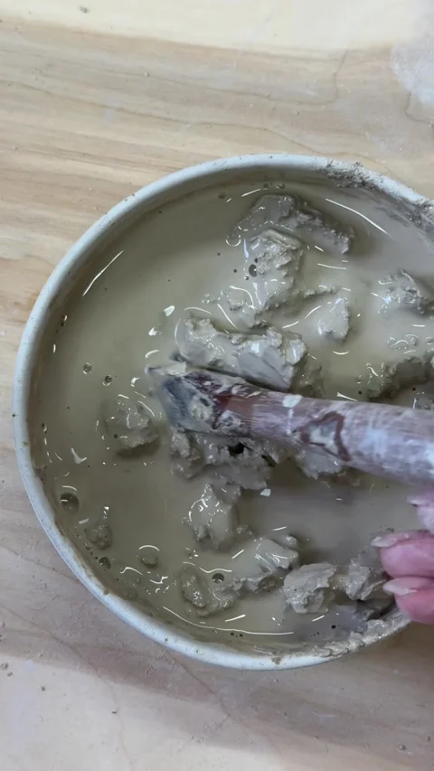 Close-up of hands mixing clay with water in a ceramic bowl to make slip. Artisti Vídeo Stock 313072571