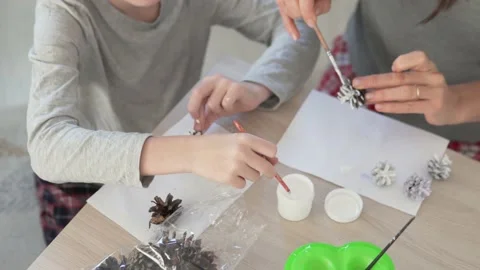 Close-up of hands, mother and son decorate spruce cones with white acrylic paint Stock Footage 145279080