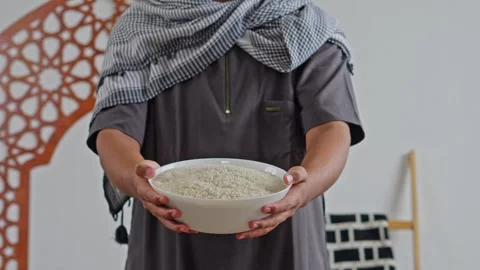 Close-up of hands offering white bowl of rice grains for zakat Al-fitr charity Stock Footage 329102826