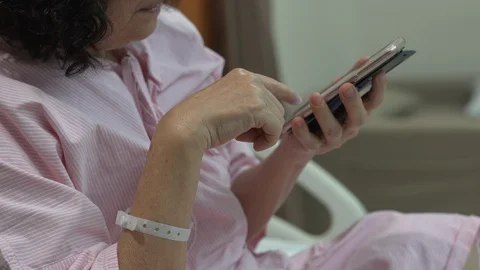 Close up hands of old woman using smartphone in hospital bed, entertainment a Video stock 107884555