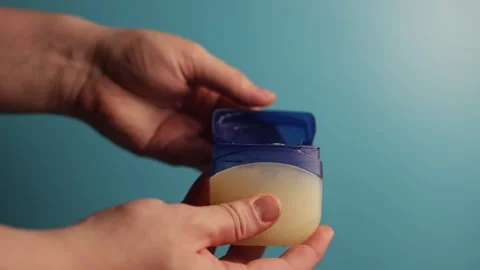 Close-up of hands opening a petroleum jelly jar against a blue background Stock Footage 340268514