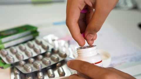 Close-up of hands opening a white pill bottle with blister packs of tablets.. Stock Footage 330547465