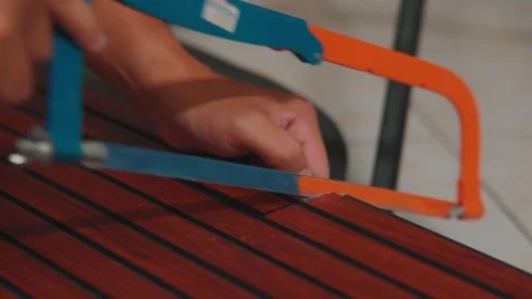 Close-up of Hands Operating a Hacksaw on a Faux Teak Decking Surface Stock Footage 333321748
