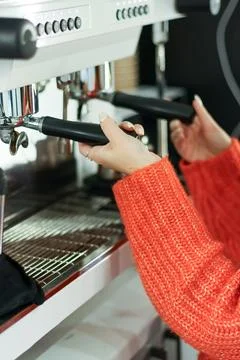 Close-up of hands in orange sweater operating espresso machine handles Stock Photos