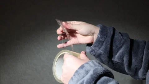 Close-up of hands peeling clear tape from a roll against a dark background Stock Footage 339180925