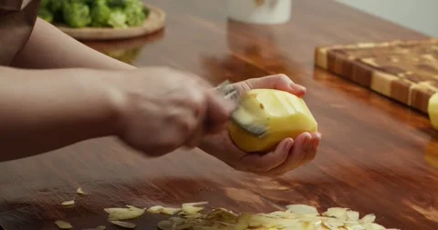 Close up of hands peeling fresh potato with peeler on wooden table, preparing Stock Footage 319342074