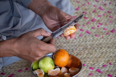 Close-up of hands peeling an orange slice with a grater on a woven mat Photos