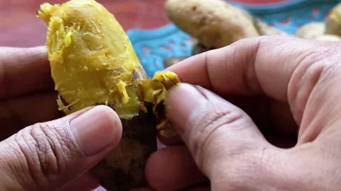 Close up of hands peeling skin off boiled yellow sweet potato Stock Footage 340050018
