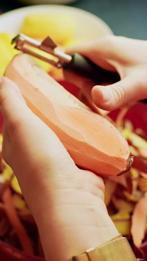 Close-up hands peeling sweet potato with a vegetable peeler over a bowl of Video stock 331111602