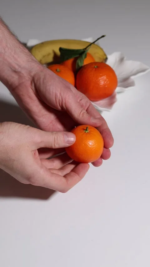 Close-up of hands peeling a tangerine, showing segments, with other fruits. Stock Footage 326978211