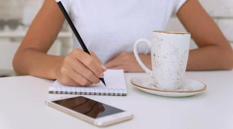 Close up of hands with pen writing to notepad with coffee and smartphone on the Stock-Fotos