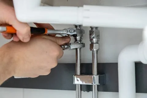 Close-up of hands performing plumbing work, tightening pipe fittings with two Stock Photos