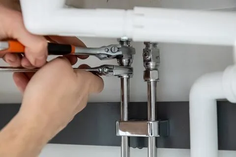 Close-up of hands performing plumbing work, tightening pipe fittings with two Stock Photos