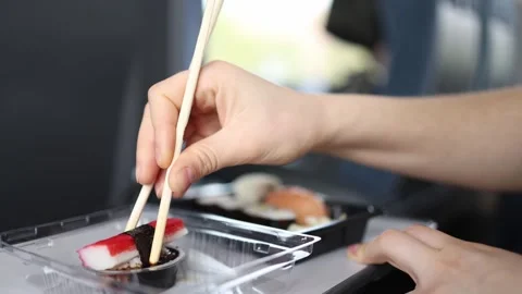Close up of hands picking fresh sushi with chopsticks on train tray table dippin Stock Footage 307699721