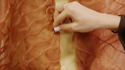 Close up of hands pinching and arranging translucent orange organza with raised Stock Footage 335313692