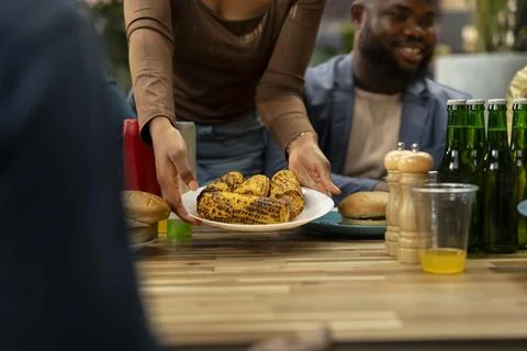 Close up of hands placing plate of grilled corn on rooftop dining table Stock Photos