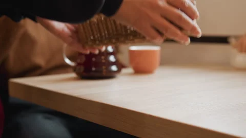Close up of hands placing woven wicker basket on wooden table with teapot and Stock Footage 344866655