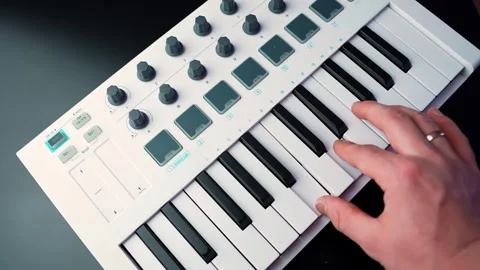 Close-up of hands playing a compact MIDI keyboard with drum pads and knobs on a Stock Footage 328588357