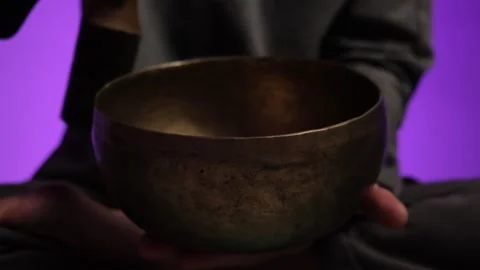 Close-up of a hands playing a Tibetan singing bowl in a dimly lit room with Stock Footage 303959954