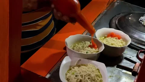 Close-up of hands pouring chili sauce from a bottle into a chicken noodle  Stock Footage 292906815