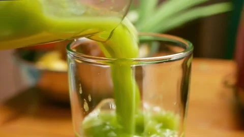 Close-up of hands pouring green leaf salad Kale smoothie into a glass. Stockbeeldmateriaal 157408882