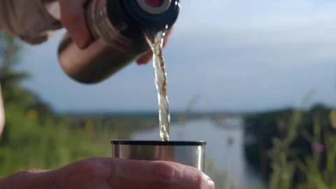 Close up of hands pouring hot drink into mug from thermos on river bank. Stock Footage 243580972